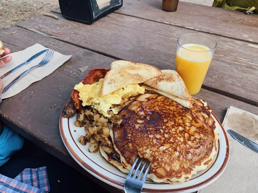huge pancakes, scrambled eggs, toast on a plate with orange juice in a glass
