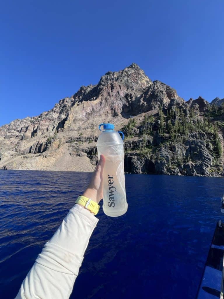 Holding a sawyer cnoc 1 liter water bottle in front of a very blue lake.
