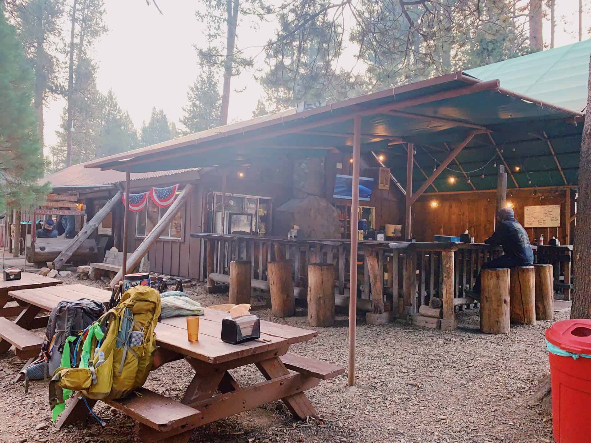 a small wooden building with a covered porch and picnic tables with backpacking packs on them at VVR in the Sierra