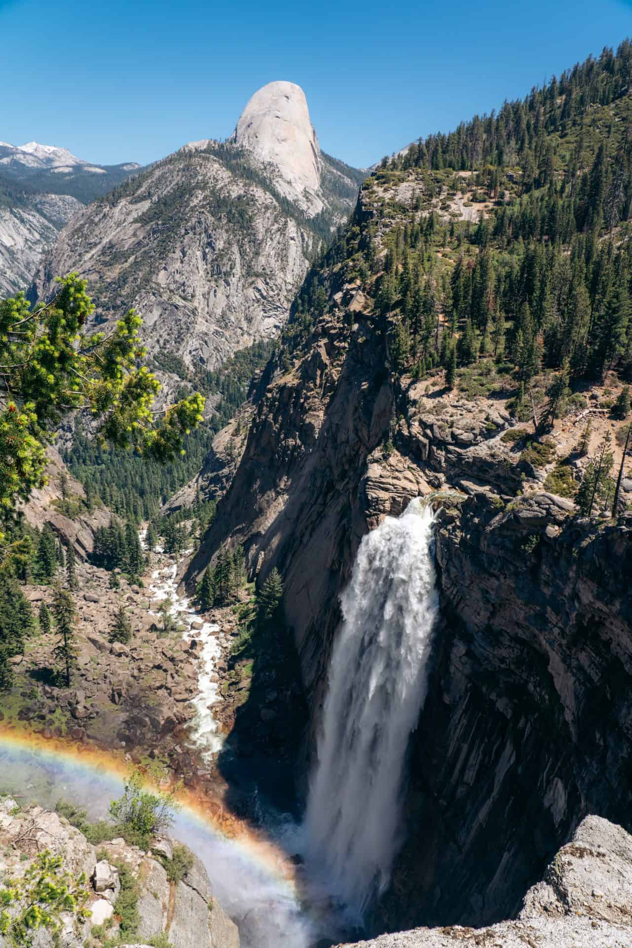 a rainbow in front of Illilouette fall in a gorge in yosemite national park with the backside of Half Dome in the distance
