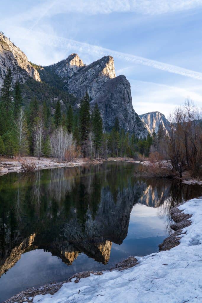 the diagonally pointed granite rock features reflect in a still river with snow covered banks