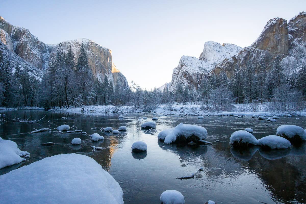 Valley View viewpoint at sunrise after a fresh snow. Rocks in river are covered in snow, El Capitan, Cathedral Rocks in the background, fresh snow