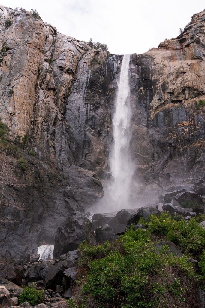 a powerful waterfall falling directly from the granite wall. Shrubs and large boulders in the foreground