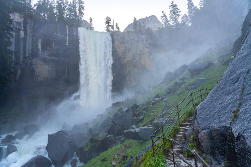 a raging white waterfall flows over a granite wall with lots of mist circling the air.