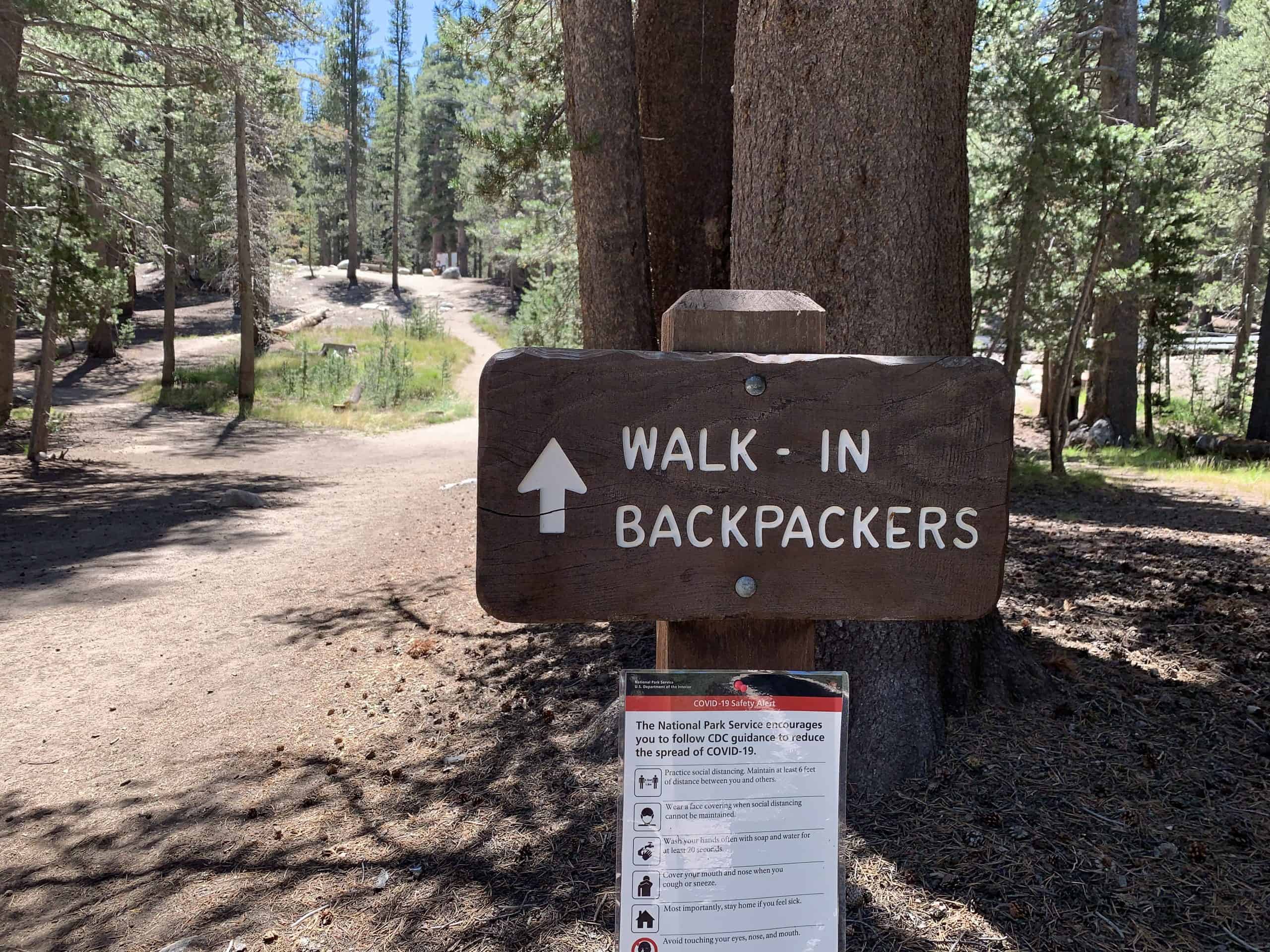 wooden sign reading "walk-in backpackers" with an arrow pointing forward. A small path up a hill is behind the sign