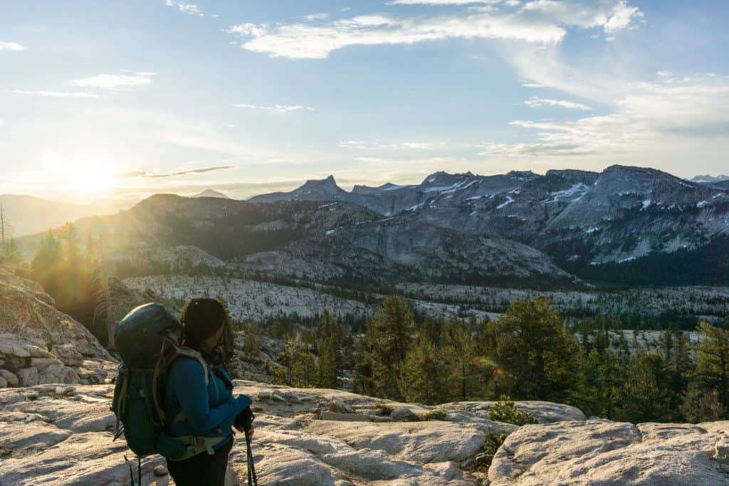 sun rising over mountains in yosemite. a woman backpacker stands to the left looking out at them