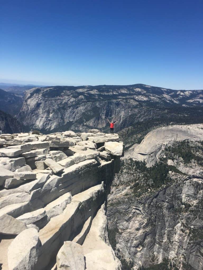 Breathtaking view from Half Dome trail in Yosemite National Park, hiker celebrating on the edge.