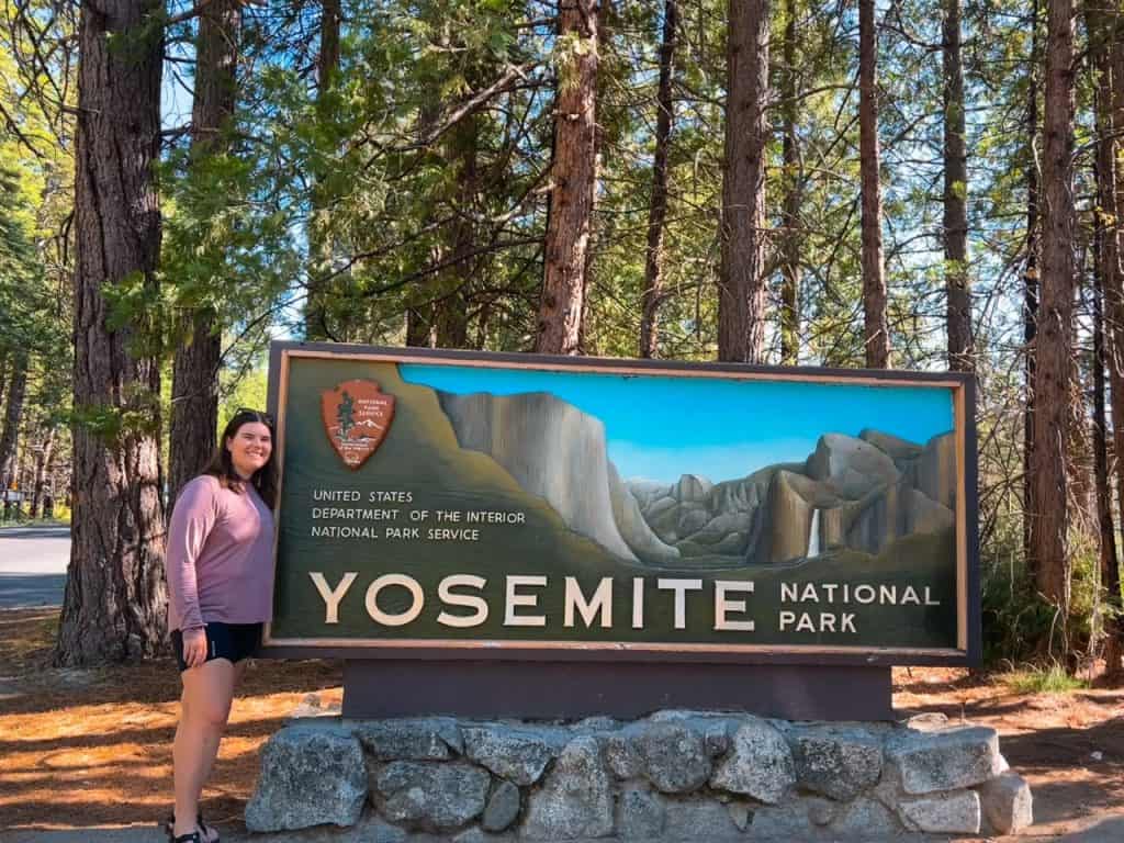 author Emily standing next to large Yosemite national park entrance sign