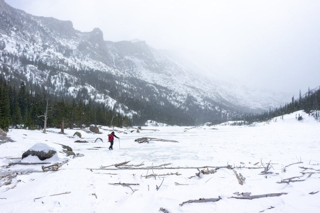 Snowy mountain landscape with a hiker in winter gear crossing a frozen lake scene.