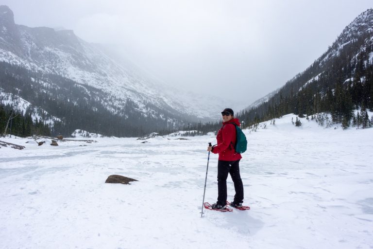 A woman snowshoeing in a scenic winter mountain landscape with snowy peaks and forests.