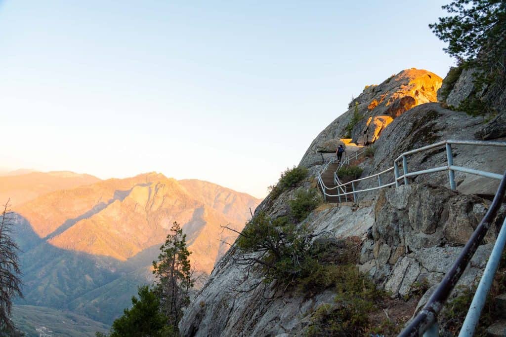 Hiking trail along a rocky cliffside in Sequoia National Park with mountain views at sunset.