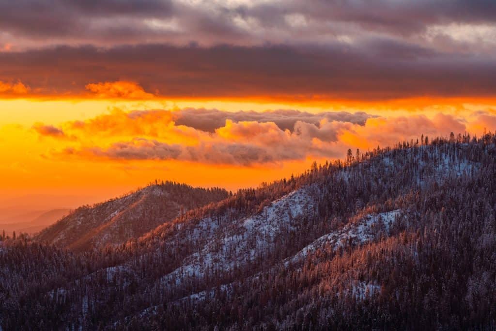 sky glowing in sunset colors above a tree-filled mountainside.