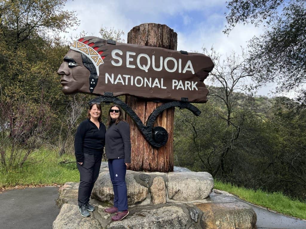 2 women standing next to the sequoia national park entrance sign at the southern entrance.
