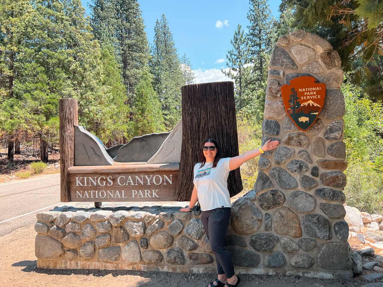 Woman standing at Kings Canyon National Park entrance sign.
