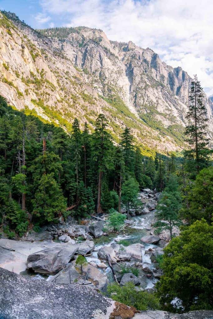 Scenic mountain river flowing through lush green forest with towering cliffs in the background. Seen from the hiking trail to Mist Falls.