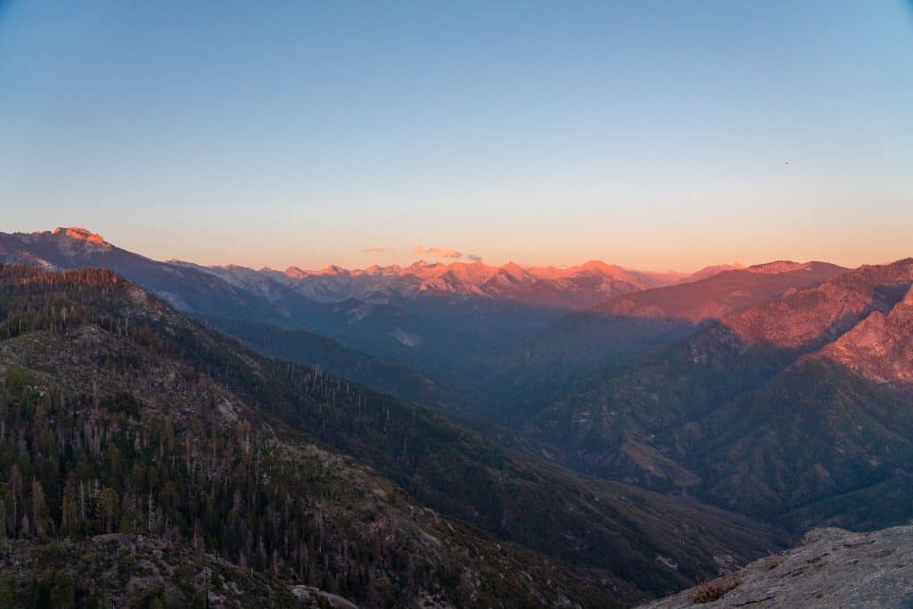 Sunset over rugged mountain landscape with forested slopes and distant peaks seen from Moro Rock in Sequoia National Park.