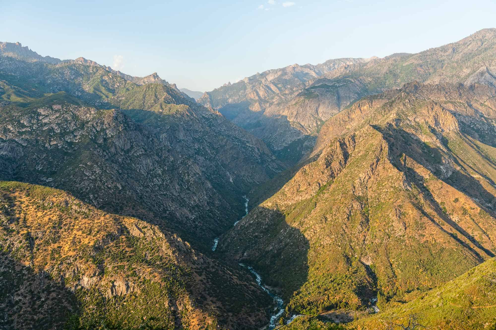 Scenic mountain valley with lush greenery and rugged peaks at sunset.